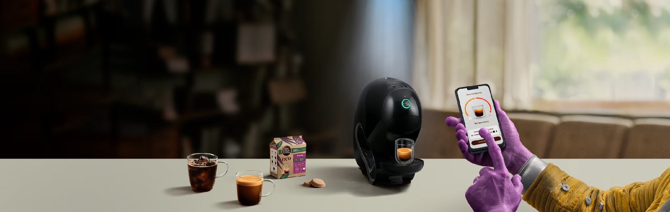 A mão de um extraterrestre a utilizar a aplicação NESCAFÉ Dolce Gusto no telemóvel para personalizar o seu café. Máquina NEO, embalagens de café e bebidas no fundo.